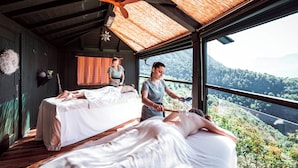 Une salle de spa équipée de deux lits, d’un ventilateur de plafond et offrant une vue sur un paysage boisé.
