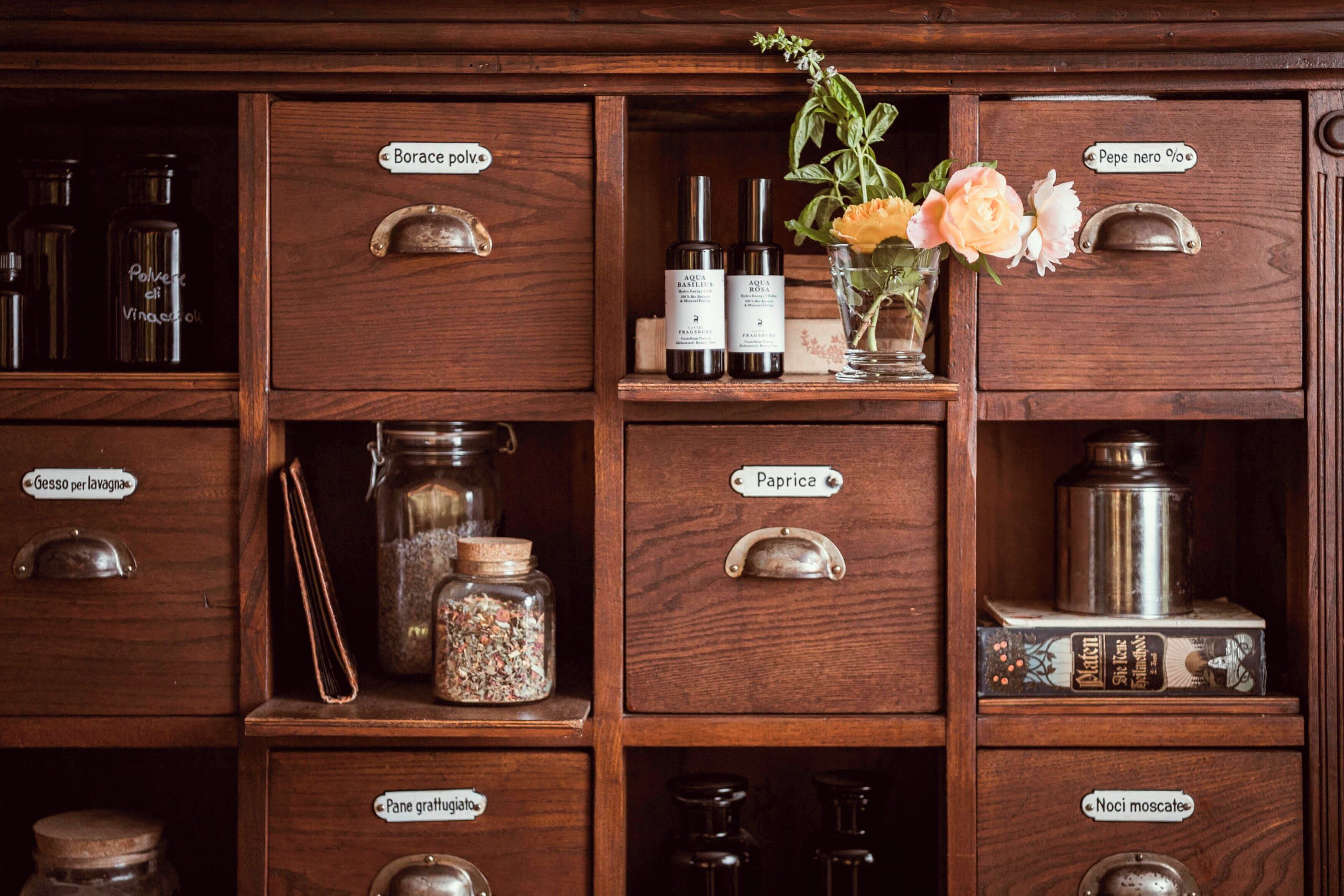 Un armario de madera con cajones etiquetados que contienen diversos utensilios de cocina como botellas, frascos y un organizador de especias.