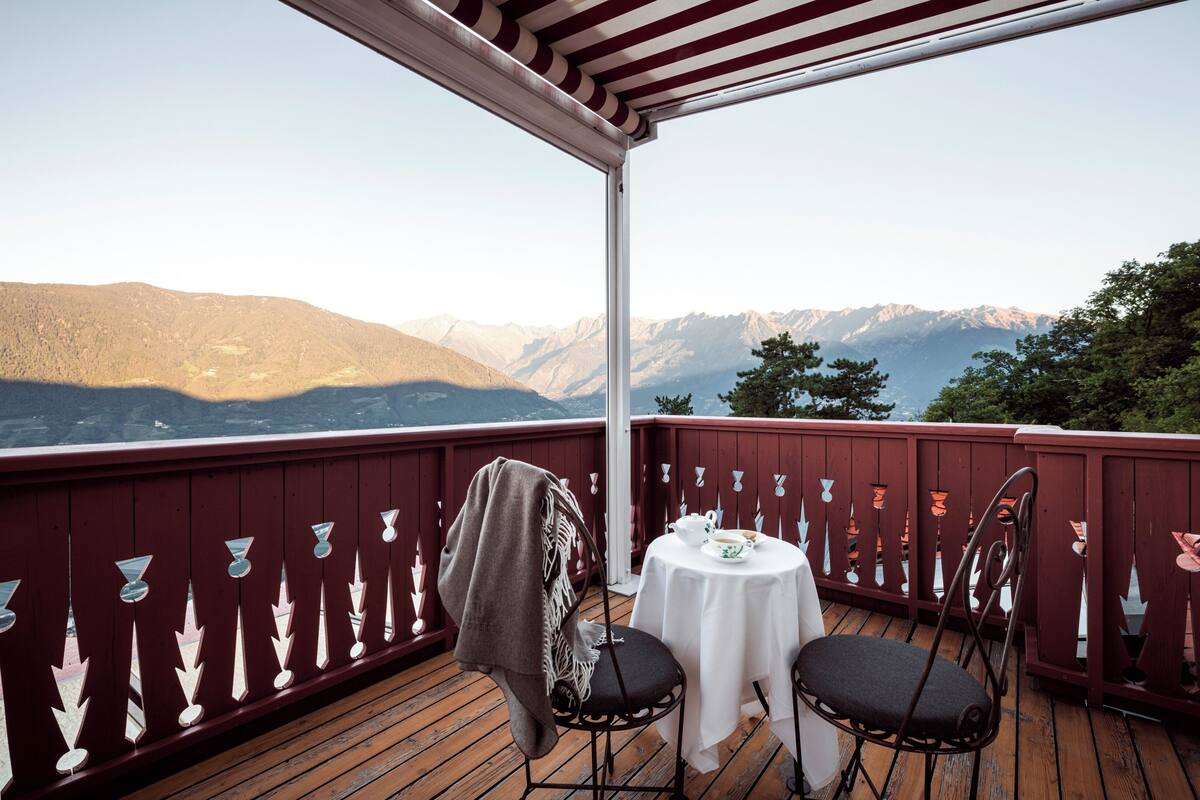 A wooden deck with a table and chairs, overlooking a mountainous landscape.