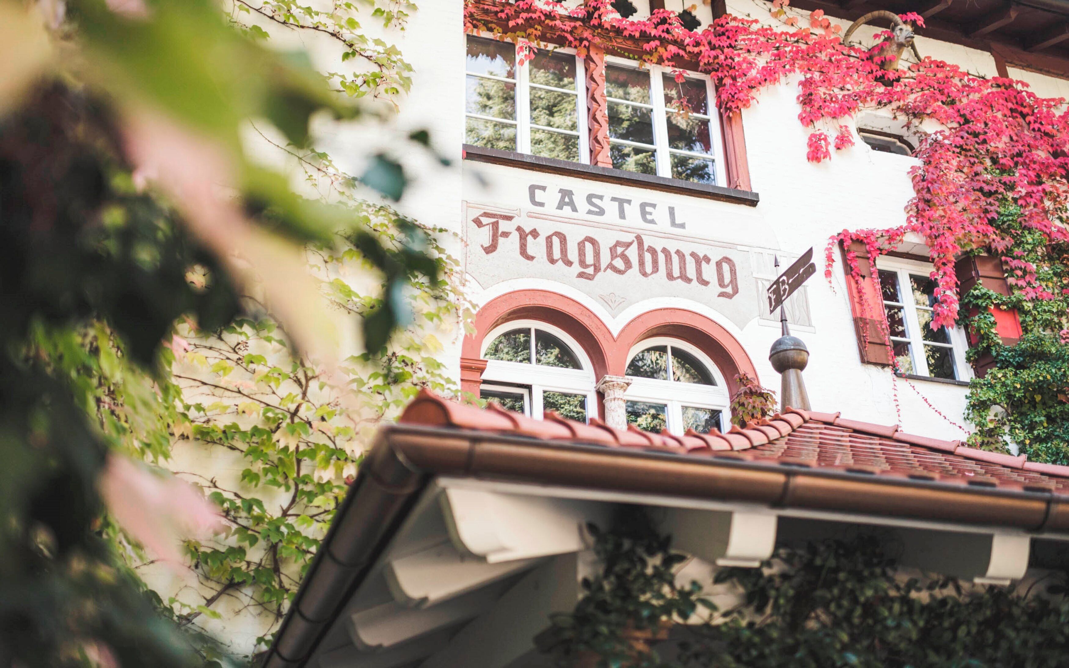 Ein Gebäude mit einem Schild, auf dem 'CASTEL Fragsburg' steht, und einem Ziegeldach.