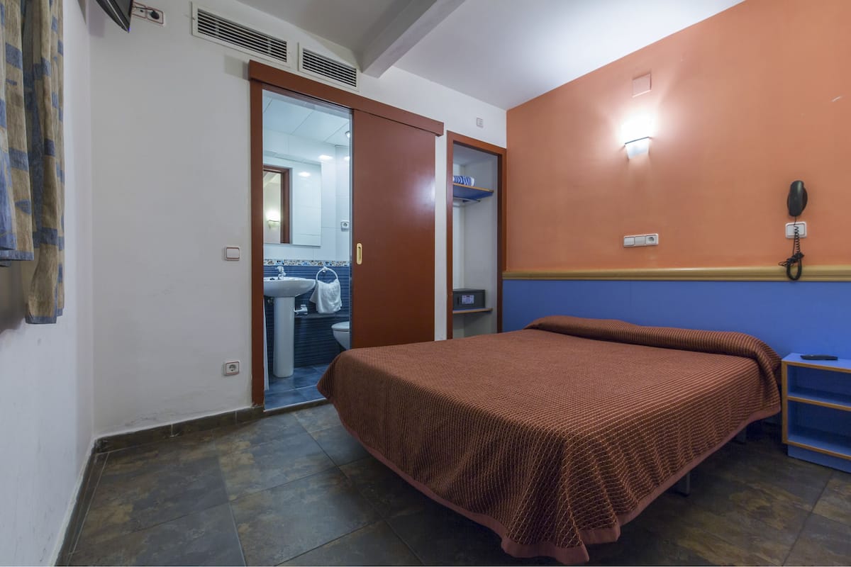 Quarto de hotel com cama, banheiro visível por uma porta aberta, telefone e prateleira.