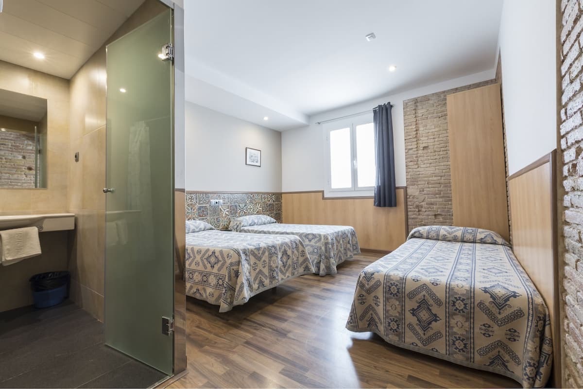 Quarto com duas camas, banheiro e parede de tijolos.
