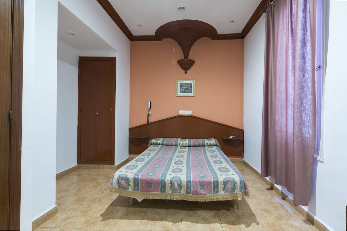 Quarto com cama, porta de madeira, telefone fixado na parede e quadro emoldurado.