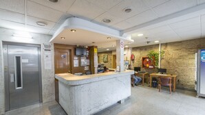 A reception area with a marble counter, a wooden desk, a fire extinguisher, and a stone wall. - Barbara (BARCELONA)