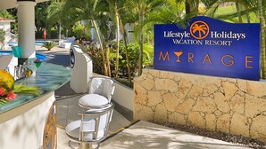 A bar area with a sign for Lifestyle Holidays Vacation Resort Mirage, a pool, and outdoor seating. - Lifestyle Crown Residence Suites - All Inclusive (Puerto Plata)