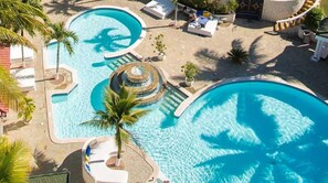 Una gran piscina al aire libre con una fuente circular, rodeada de sillas de descanso y palmeras.