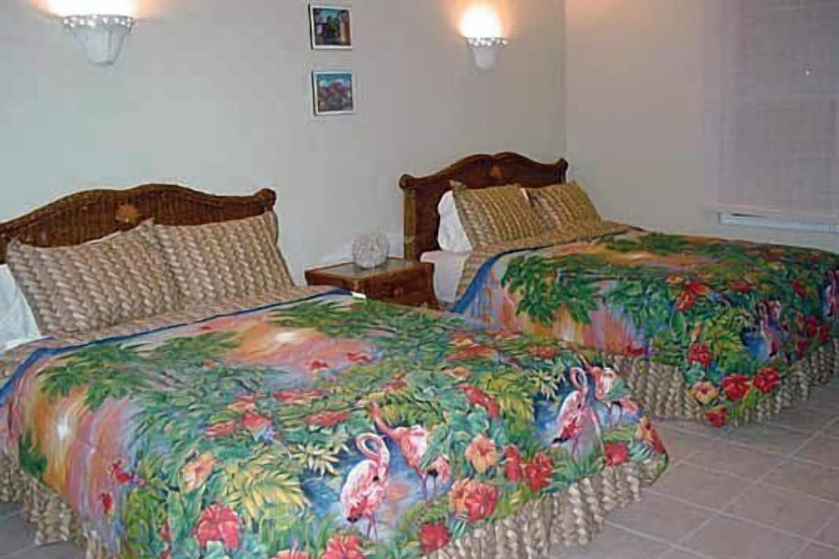 Two beds with floral bedding, a nightstand, and wall sconces.