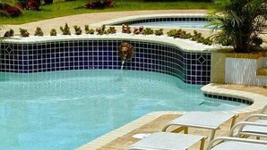 Una piscina con borde de azulejos, una fuente de agua y sillas de descanso.