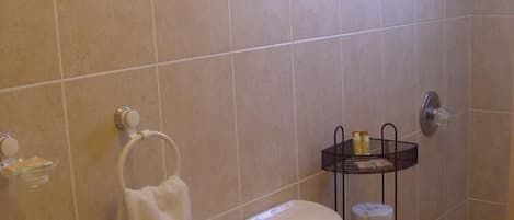 A bathroom with a toilet, sink, and shower. There is a towel rack and a shelf with toiletries.