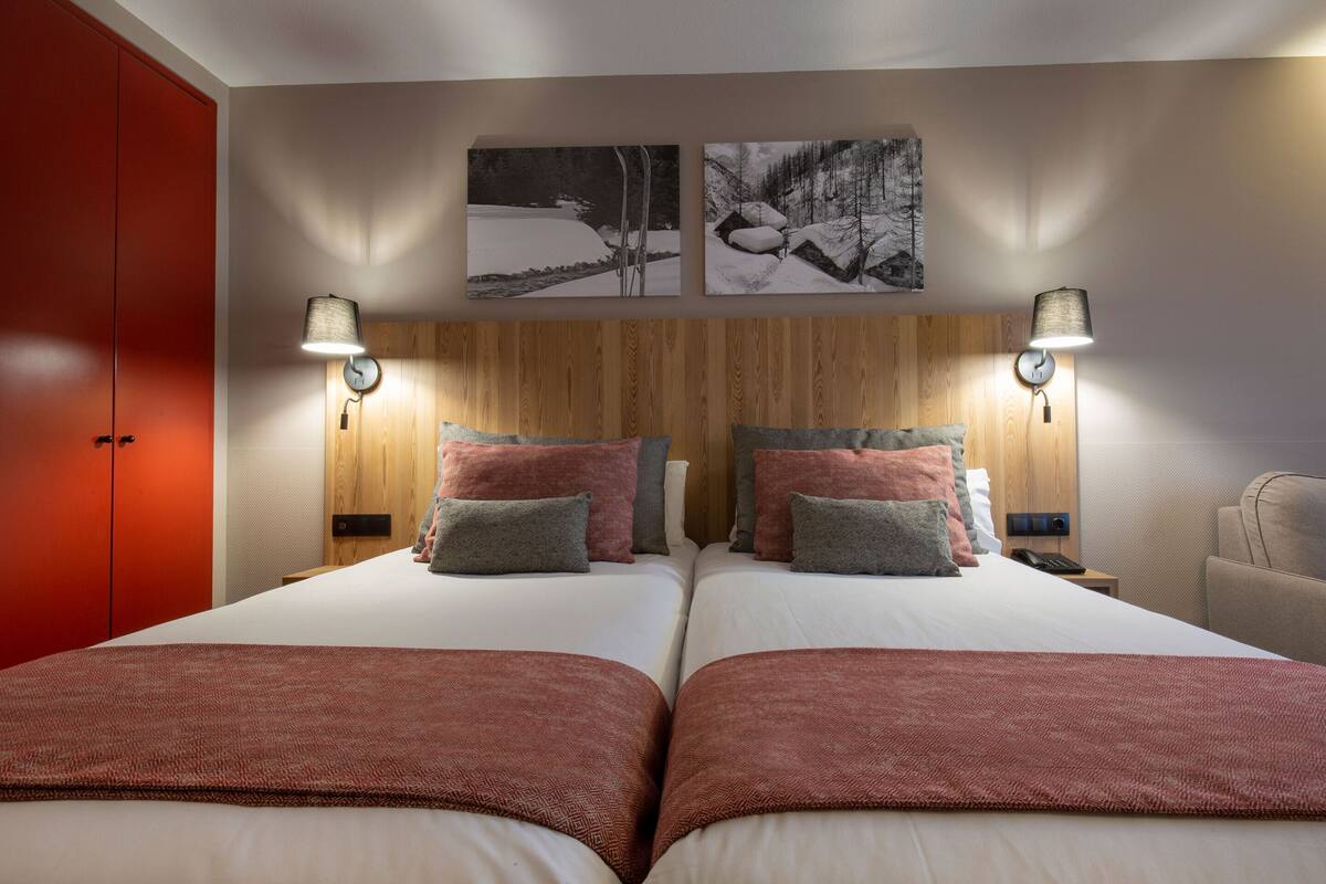 A hotel room with two beds, a wooden headboard, wall-mounted lamps, and a red wardrobe.