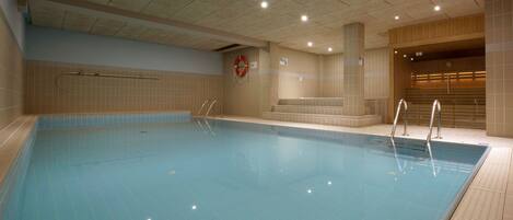 Una piscina interior con agua cristalina, paredes con azulejos y un flotador en la pared.