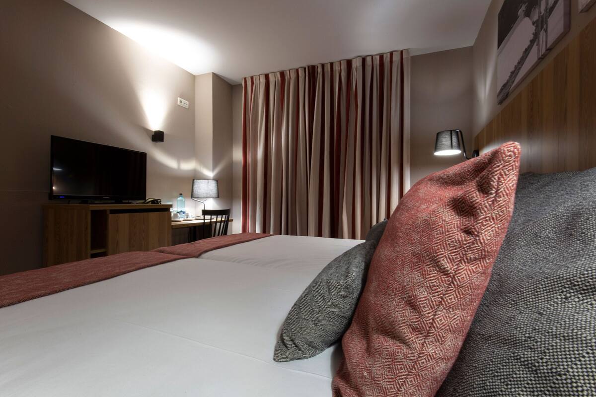 A hotel room with a bed, a desk with a computer, a TV, and a lamp.