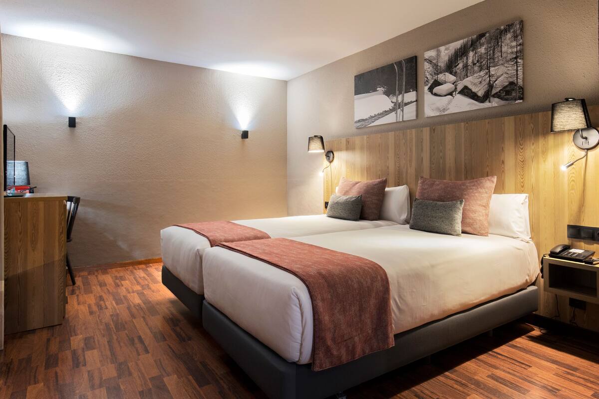 A double bed with a wooden headboard, two bedside tables with lamps, a desk with a chair, and a wall-mounted TV.