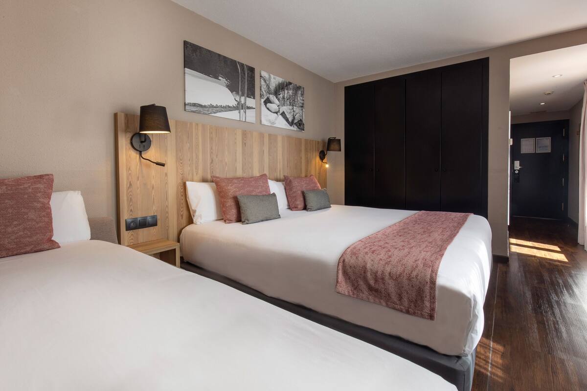 A hotel room with two beds, a wooden headboard, wall-mounted lamps, and artwork.