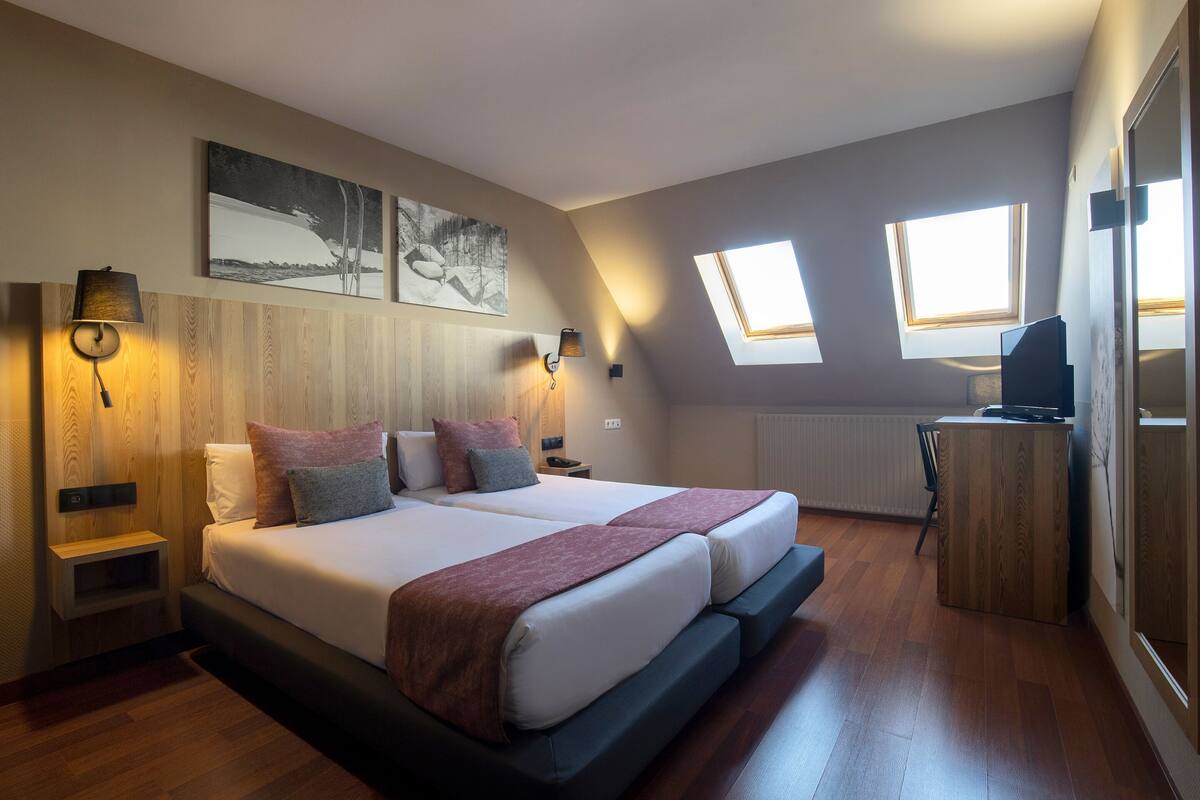 A bedroom with a large bed, two bedside tables, a desk, and a window.