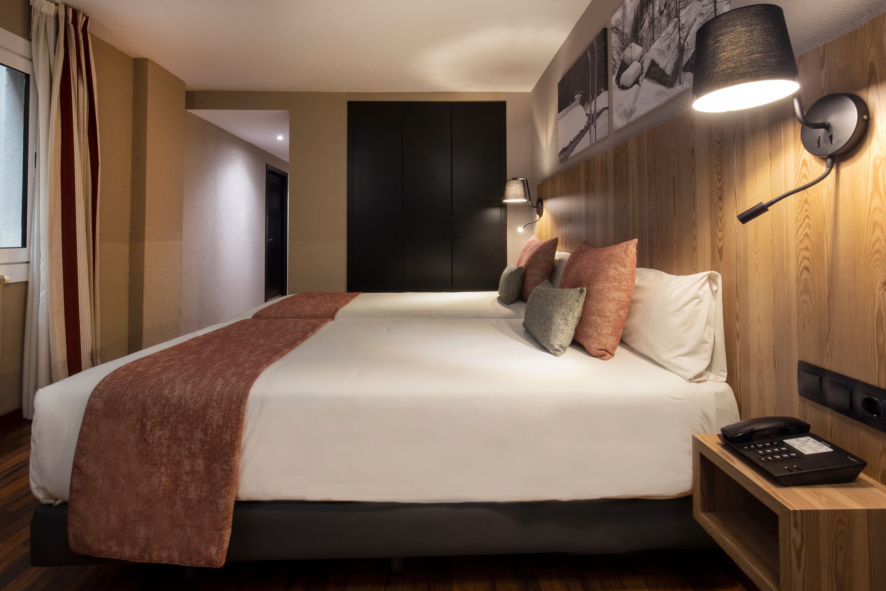 A hotel room with a bed, bedside table, lamp, and a painting on the wall.