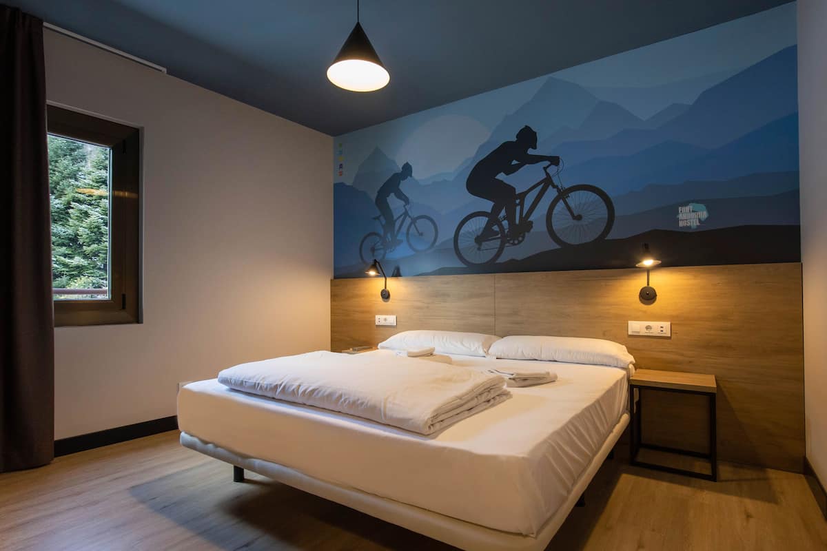 Una habitación de hotel moderna con una cama grande, un mural con temática de montaña y una ventana con cortinas.