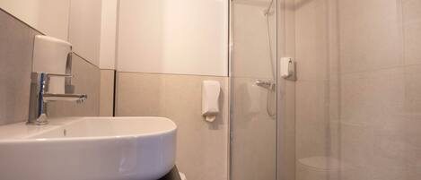 A modern bathroom with a white sink, a glass-enclosed shower, and a towel dispenser.