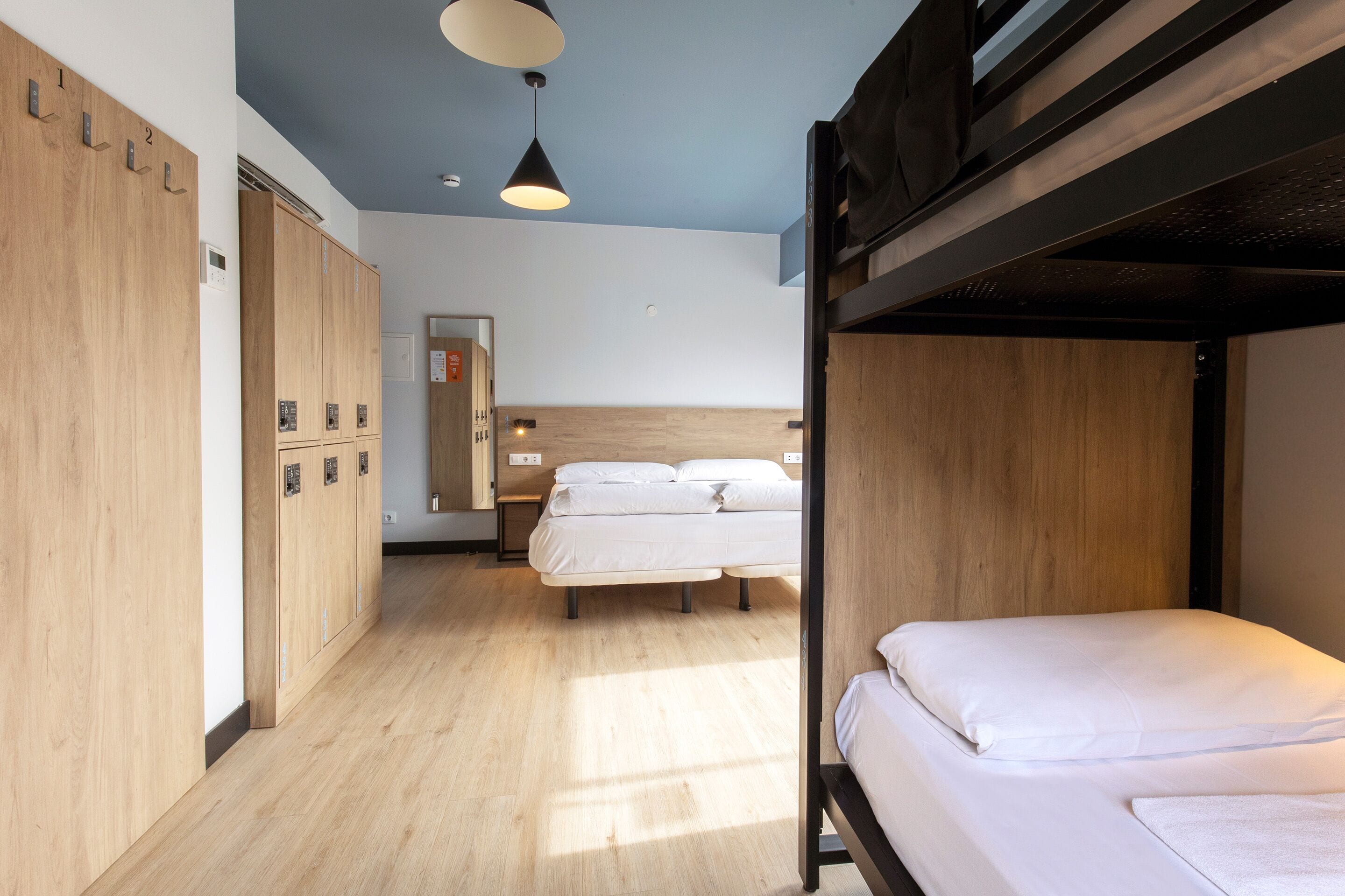 A bunk bed room with wooden lockers, a bed with white bedding, and a pendant light.