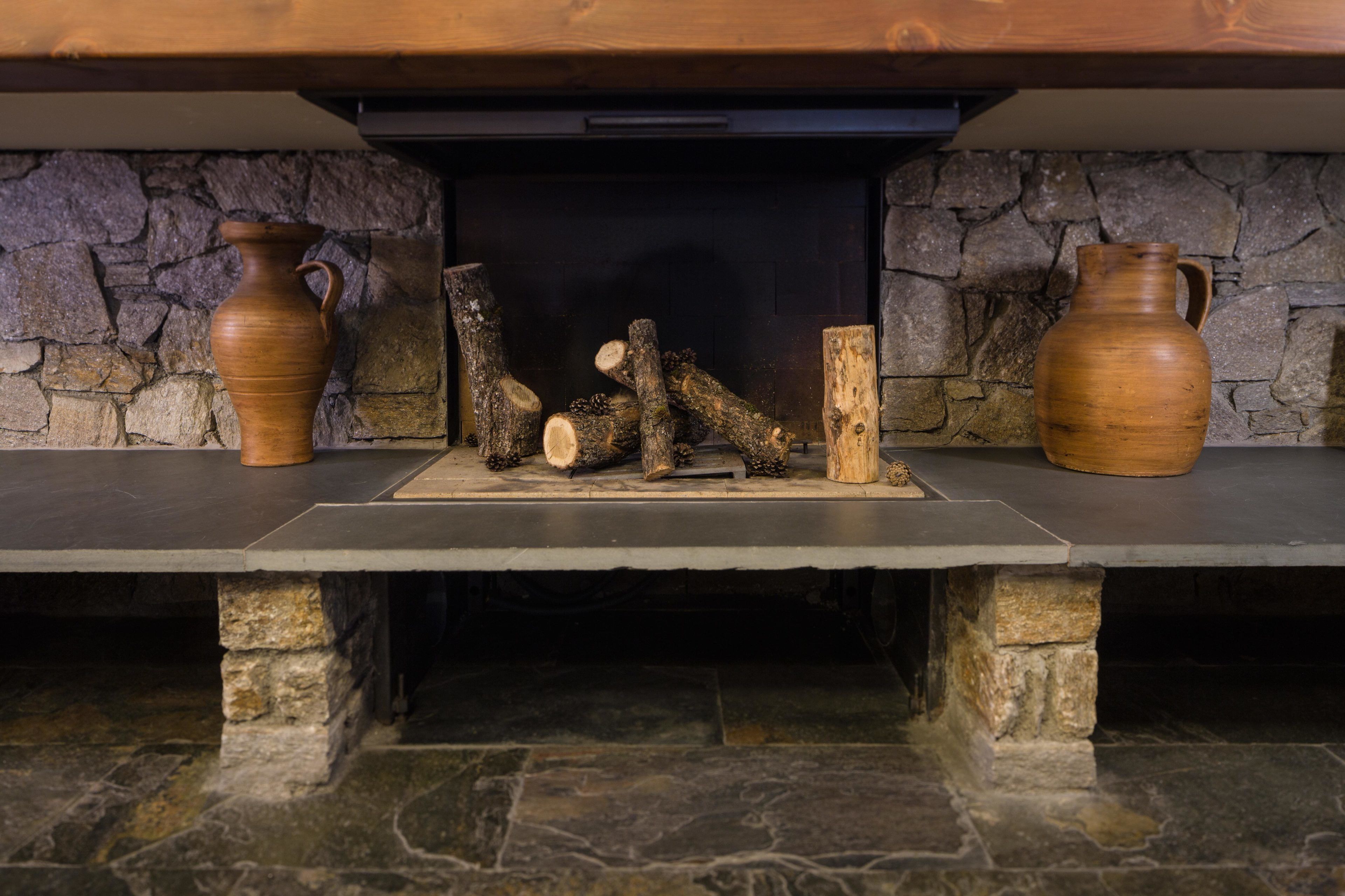 A stone fireplace with two wooden vases on either side and logs in front.