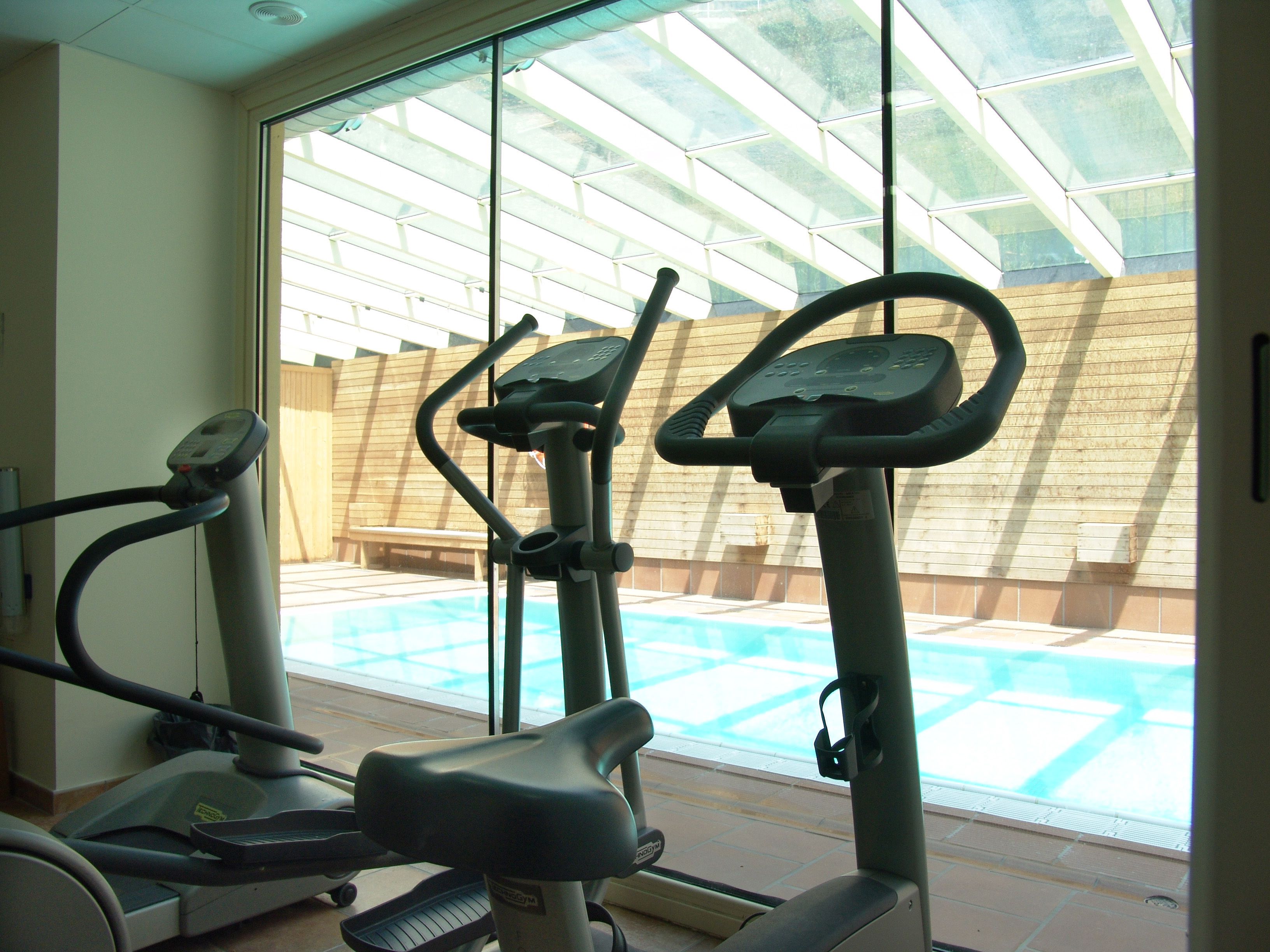 An indoor exercise area with stationary bikes and a view of an outdoor swimming pool through large windows.