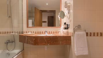 A bathroom with a marble sink, a mirror, a towel rack, a handheld showerhead, and a bathtub.