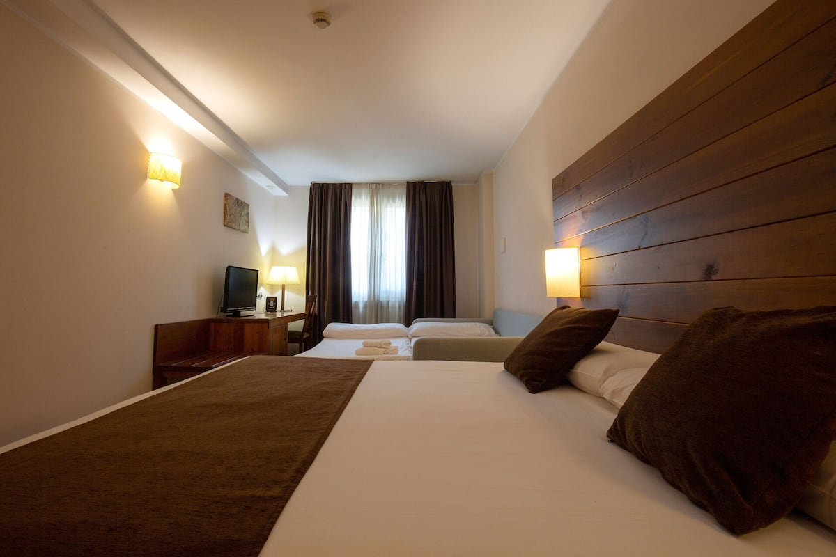 Une chambre d’hôtel avec deux lits, une télévision et des lampes fixées au mur.