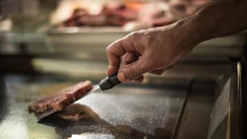 A hand holding a knife, cutting meat on a stainless steel surface.