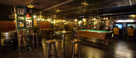Un bar con suelos de madera, taburetes y una mesa de billar.