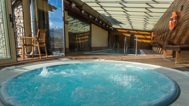 Een jacuzzi-gedeelte met een stenen muur, een houten terras en een glazen deur die leidt naar een zwembad.