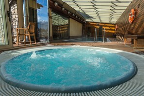 Un espace avec un jacuzzi, agrémenté d’un mur en pierre, d’une terrasse en bois et d’une porte vitrée donnant accès à une piscine.