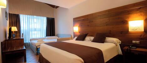 A hotel room with a large bed, a desk, a chair, a lamp, and a wooden headboard.