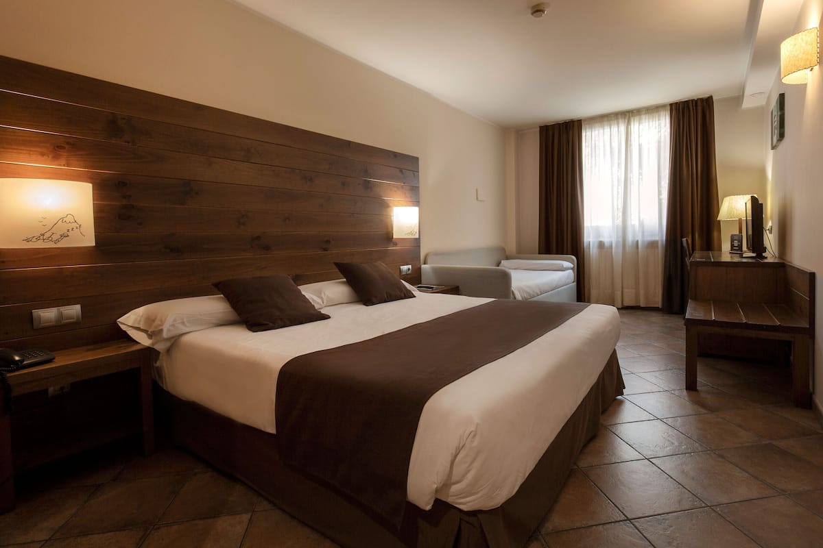 Une chambre d’hôtel avec un grand lit, une tête de lit en bois, une table de chevet avec une lampe, une commode et un bureau avec une lampe.