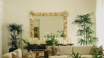 A living room with a sofa, a coffee table, and a mirror. There are plants and candles on the table.