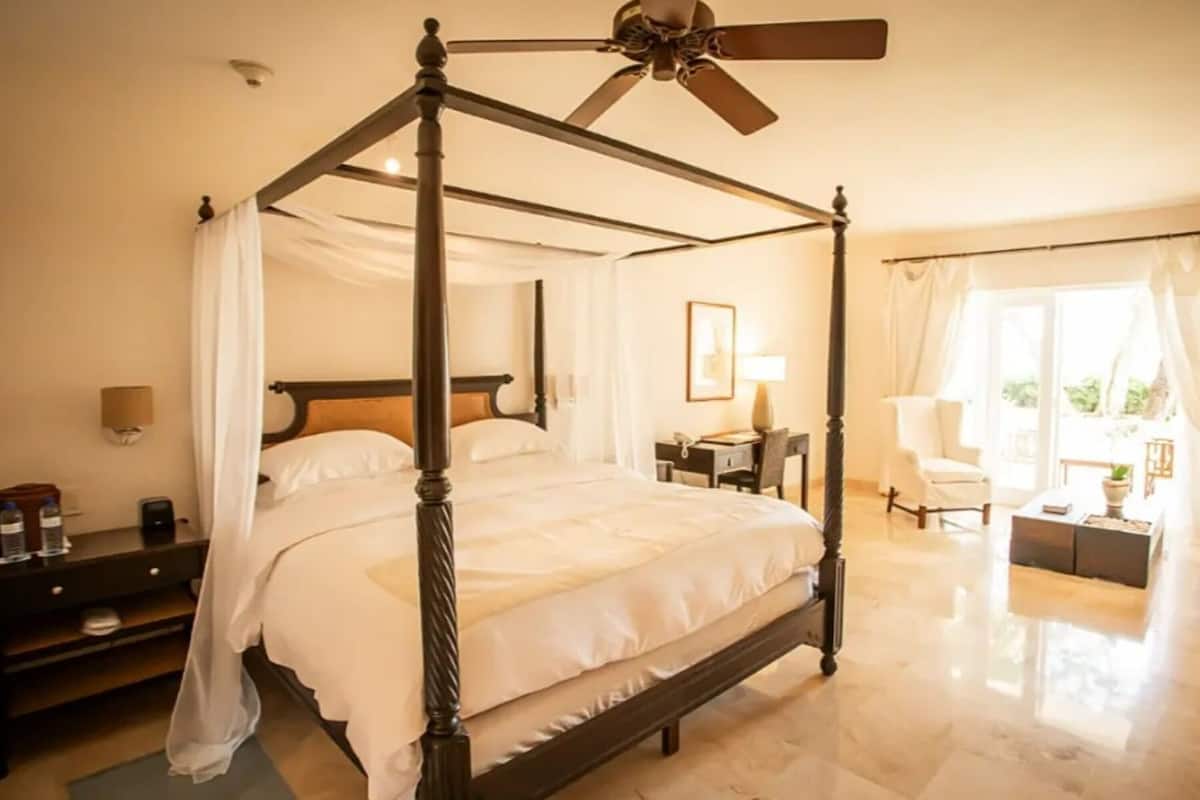 Un lit à baldaquin avec un ventilateur de plafond, une table de chevet, une lampe et une vue sur l’extérieur par une fenêtre.