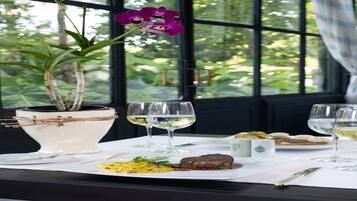 Una mesa de comedor con mantel blanco, dos copas de vino, un plato con comida y una orquídea en maceta.