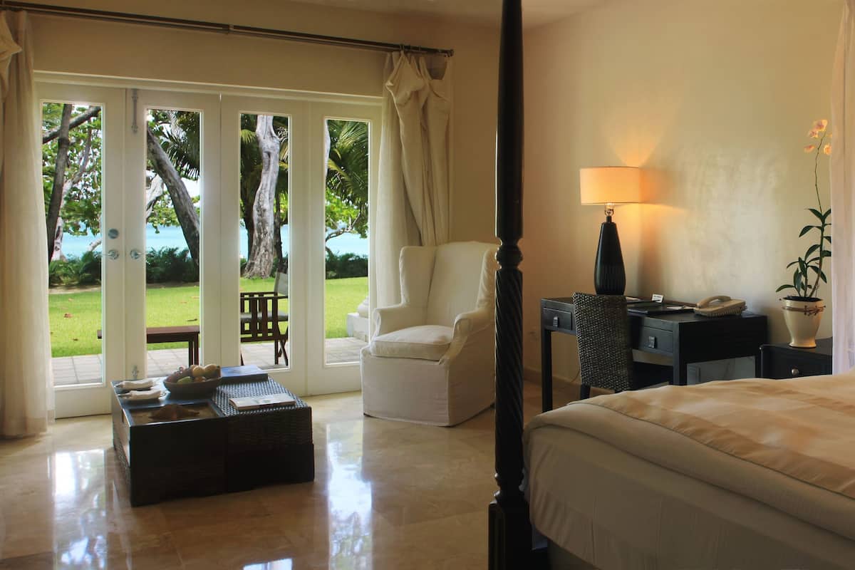 Une chambre à coucher avec un lit à baldaquin, un bureau avec une lampe et une vue sur un jardin, accessible par une porte-fenêtre coulissante.