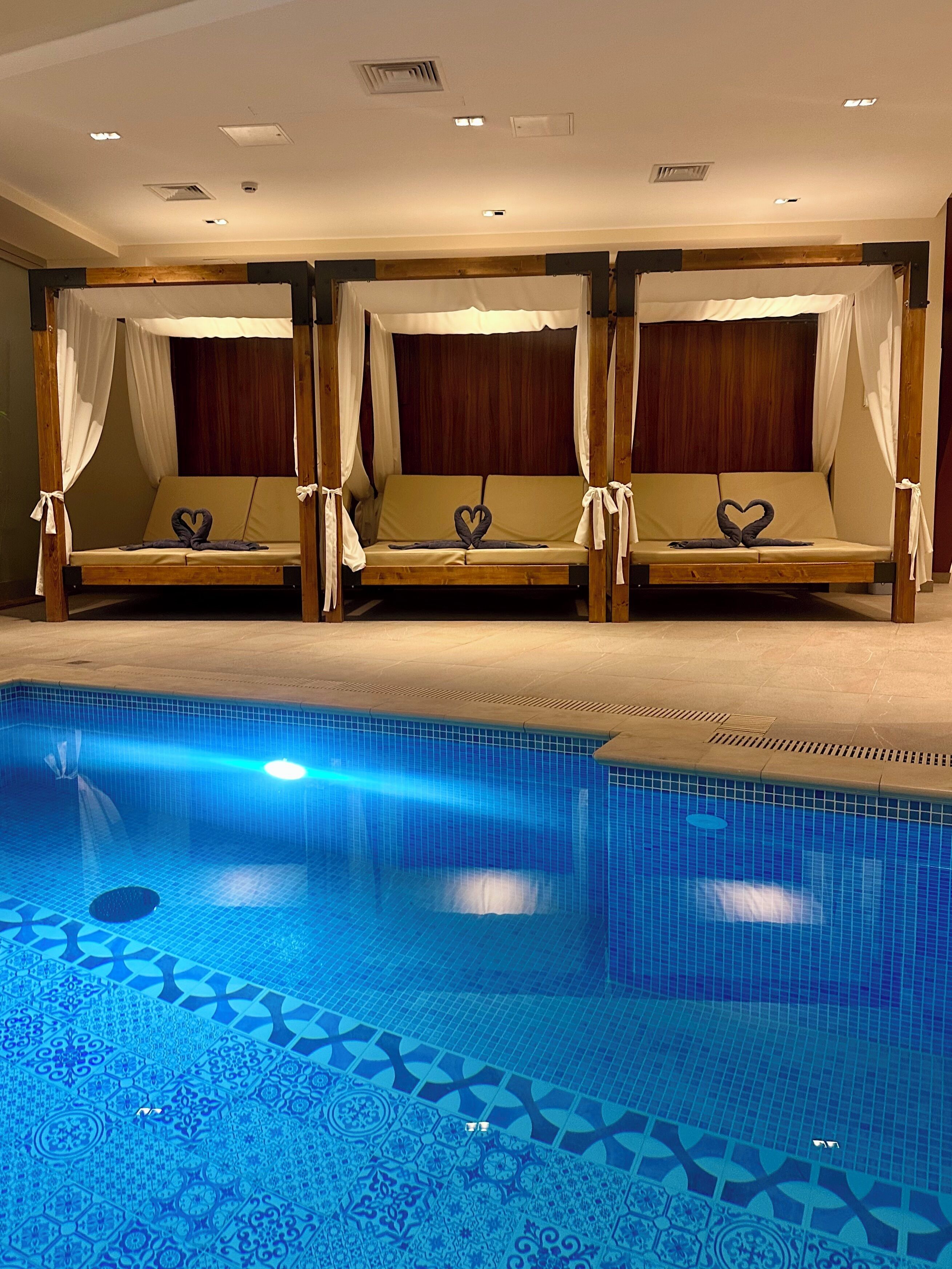 A pool area with three wooden beds with white canopies, each with a heart-shaped towel.