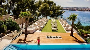 A poolside area with a wooden deck, lounge chairs, and a view of the sea. - Hotel Eden (Podstrana)