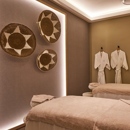 A spa room with two beds, towels, and wall-mounted robes.
