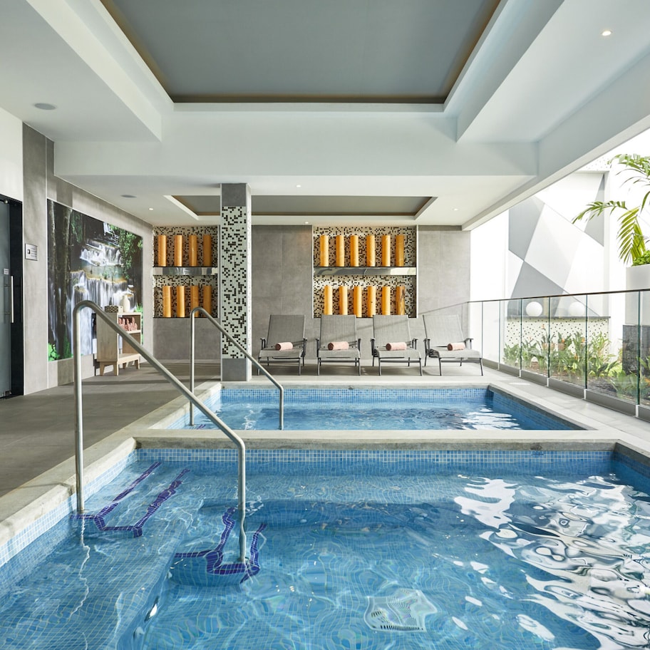 A modern indoor swimming pool with clear blue water, a glass railing, and a view of the sky.