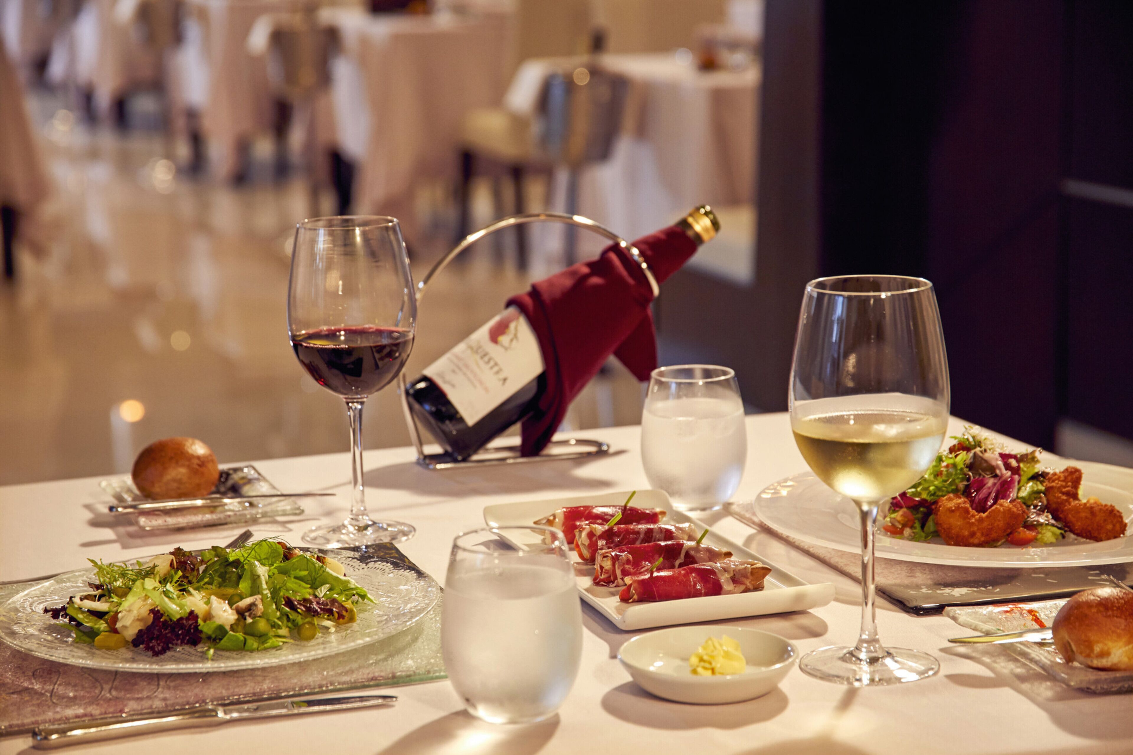 A dining table with various dishes, glasses of wine, and a bottle of wine.