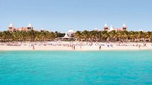 A beach resort with white domed buildings, palm trees, and a sandy beach with people and sun loungers. - Hotel Riu Palace Riviera Maya - All Inclusive (Playa del Carmen)