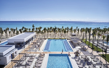 A resort with a large pool, beach view, and palm trees.