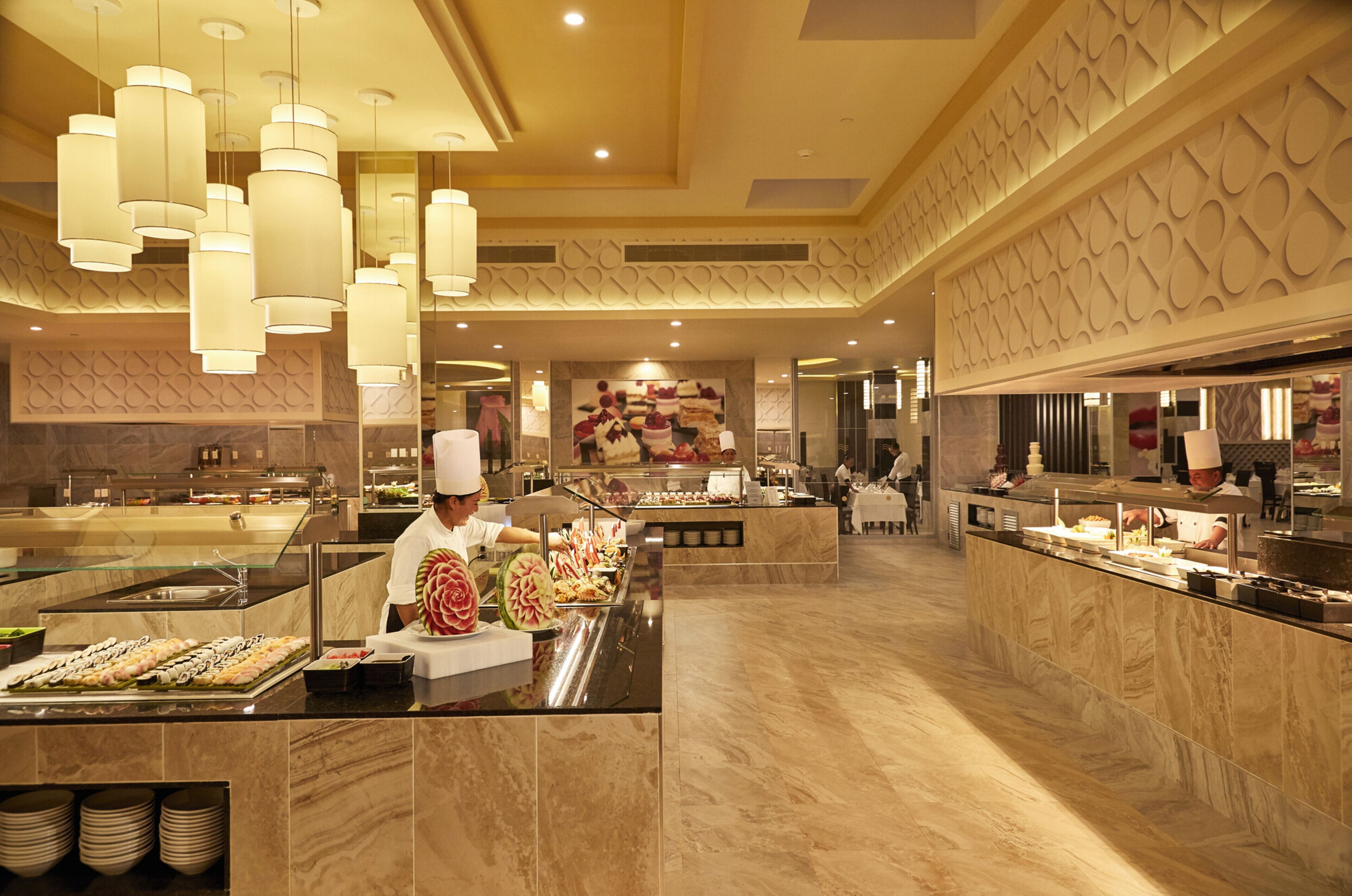 A buffet area with a chef preparing food, marble flooring, and modern pendant lighting.