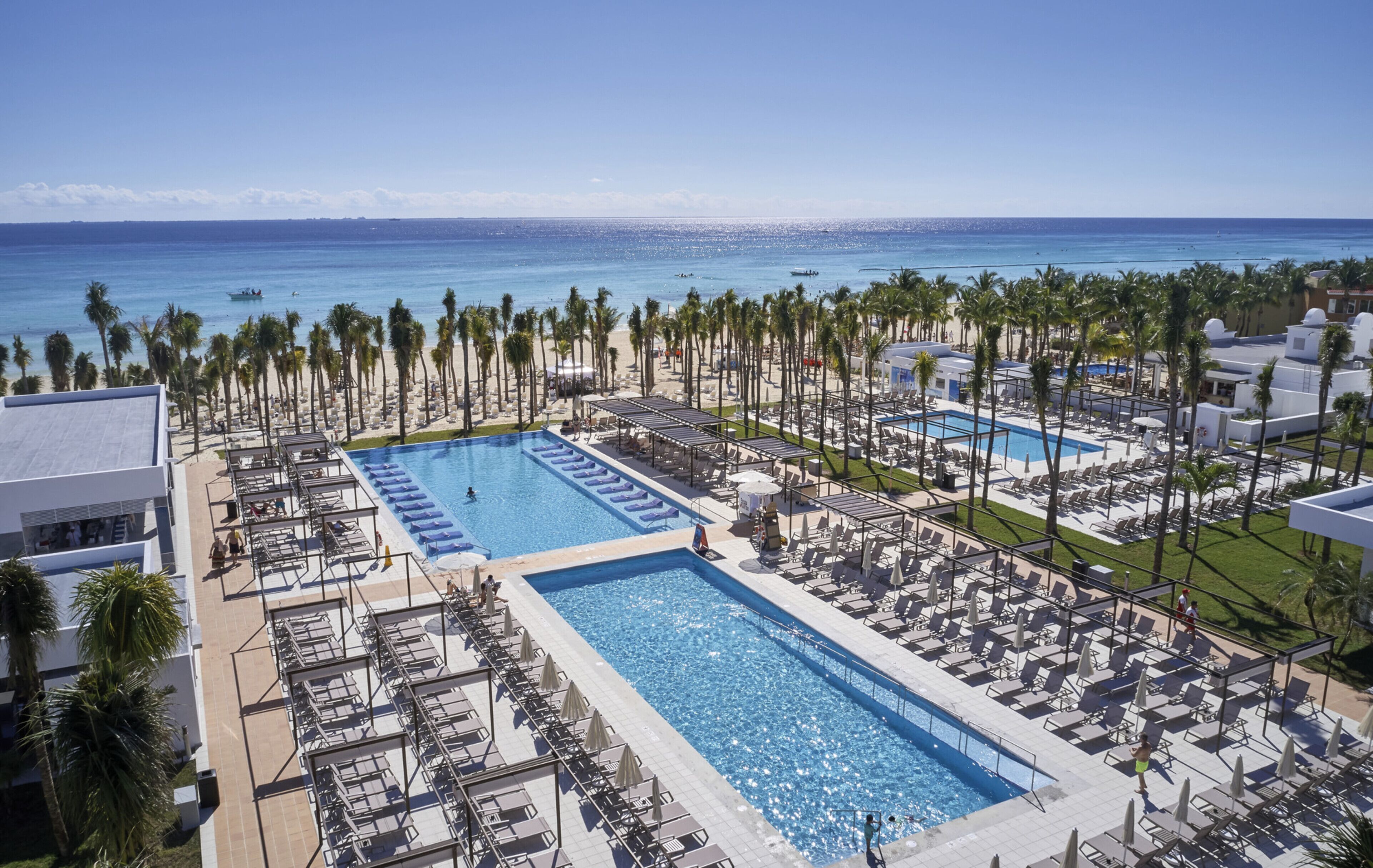 A resort with two swimming pools, palm trees, and a beach view.