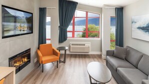 A modern living room with a fireplace, a sofa, a chair, and a TV mounted on the wall. - Harrison Beach Hotel (Harrison Hot Springs)