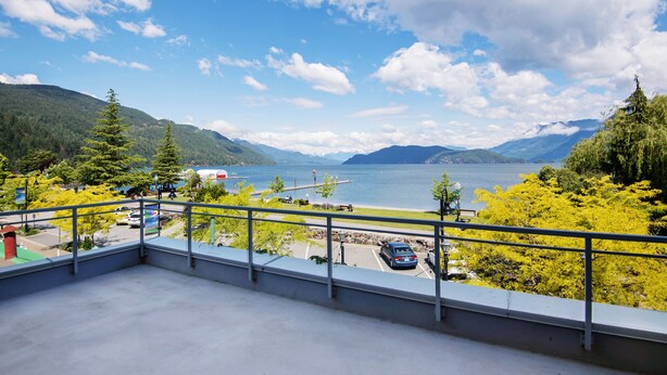 A balcony with a view of a lake, mountains, and a parking area. - Harrison Beach Hotel (Harrison Hot Springs)