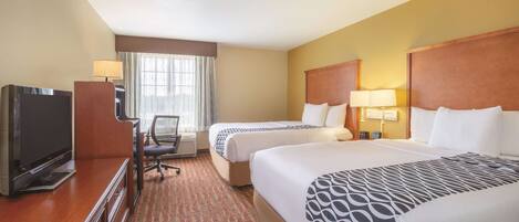 A hotel room with two beds, a desk with a TV, a chair, and a window with curtains.