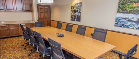 A conference room with a long table, six chairs, and a carpeted floor.